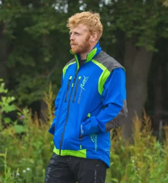 Mann in Blauer Forstjacke steht vor einem Wald