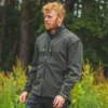 Mann in olivefarbener Forstjacke steht vor einem Wald