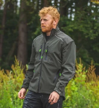 Mann in olivefarbener Forstjacke steht vor einem Wald