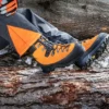 Detailansicht von Mann der auf Baumstamm sitzt. Man sieht Forstschuhe in Orange