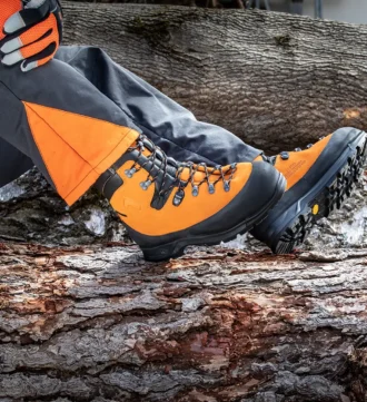 Detailansicht von Mann der auf Baumstamm sitzt. Man sieht Forstschuhe in Orange