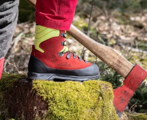 Fuß mit Forststiefel auf einem Mosbewachsenen Stein, daneben eine Axt im Baumstamm