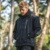 Mann in schwarzer Forstjacke steht vor einem Wald