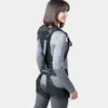 Seitliche Ansicht einer Frau in grauem Oberteil, die ein schwarzes Auxivo Exoskelett trägt, das ihren Rücken und ihre Hüften unterstützt.