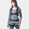 Frontale Ansicht einer Frau in grauem Oberteil und grauer Hose, die ein schwarzes Auxivo Exoskelett trägt, das ihren Rücken und ihre Hüften unterstützt